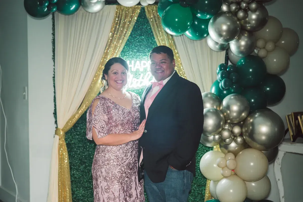 A man and a woman are posing for a picture in front of balloons.