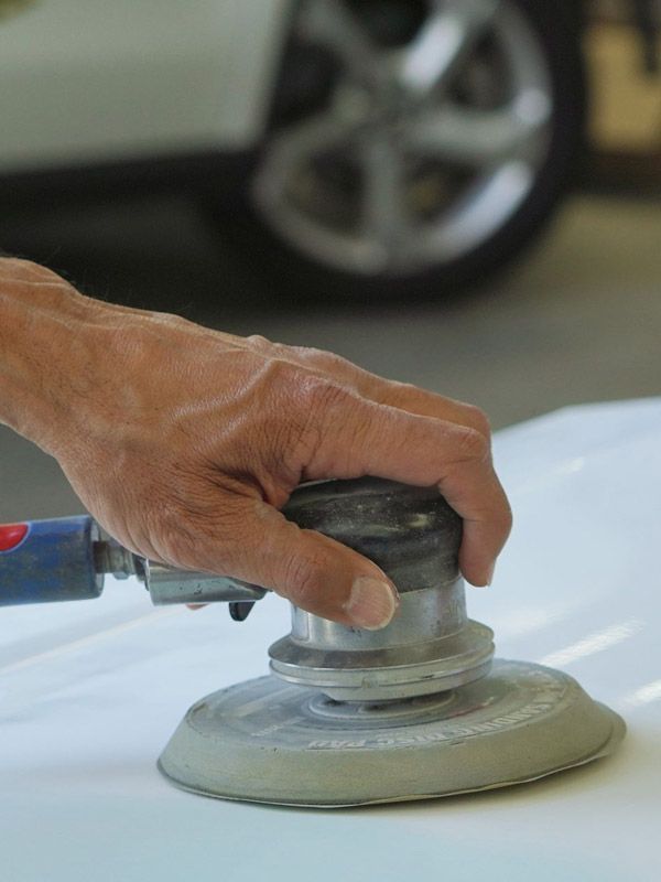 Sanding a repaired car hood.