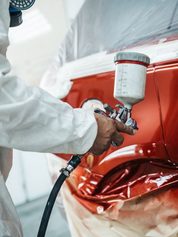 Auto paint professional spraying candy red paint on a car fender.
