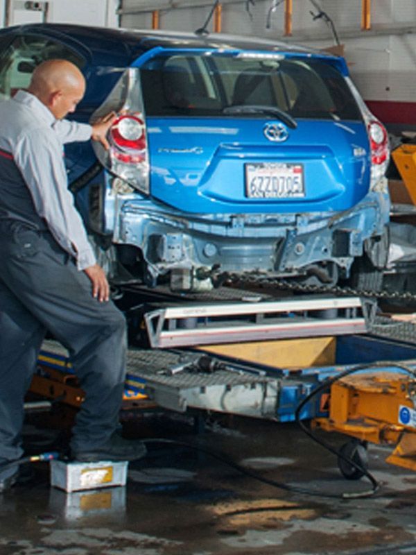 Technician straightening the rear sub-frame on a blue Toyota.,
