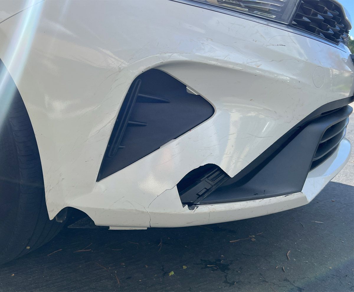 Cracked and damaged front bumper on a white Kia.