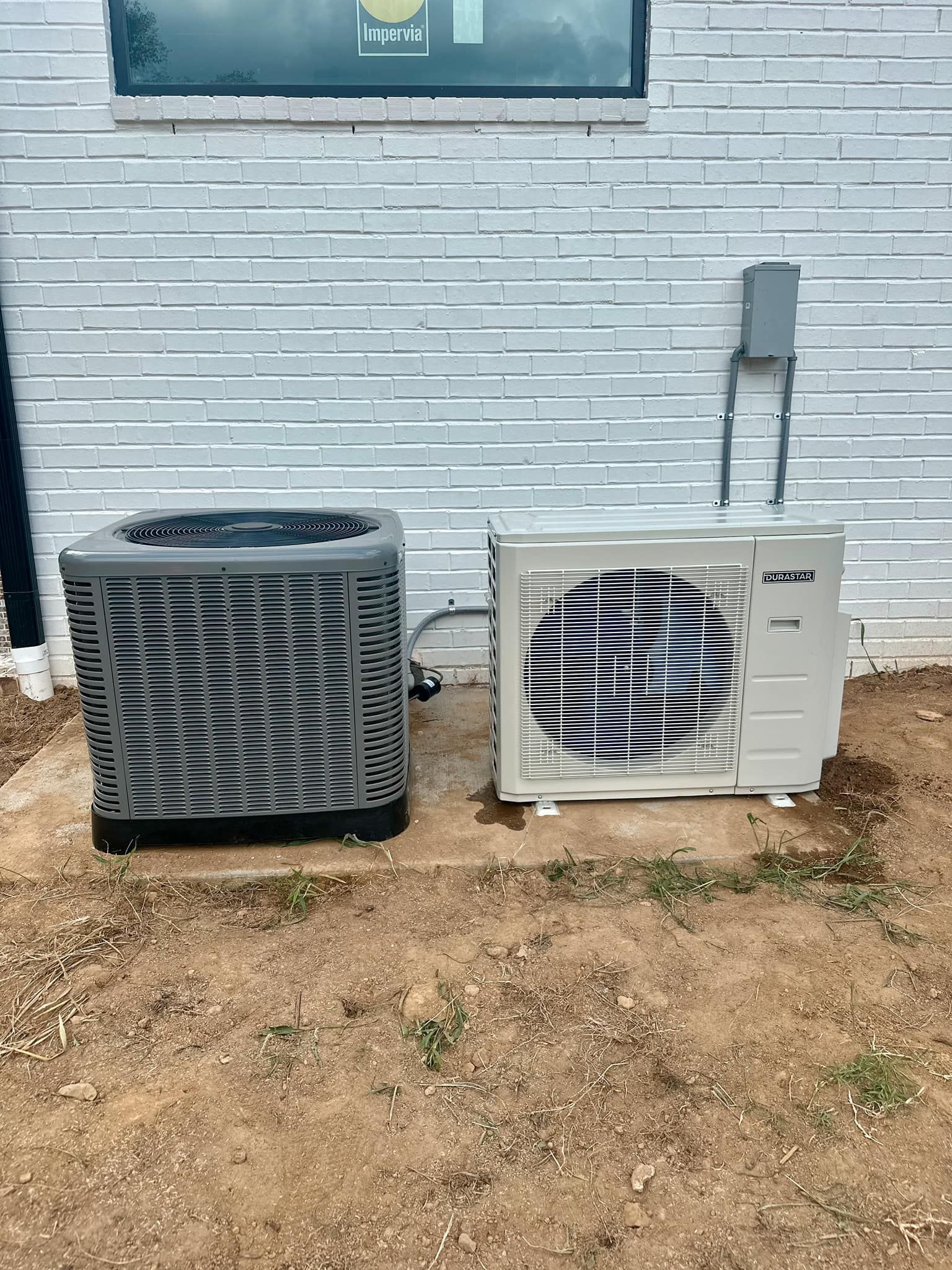 Two air conditioners are sitting next to each other on the side of a building.
