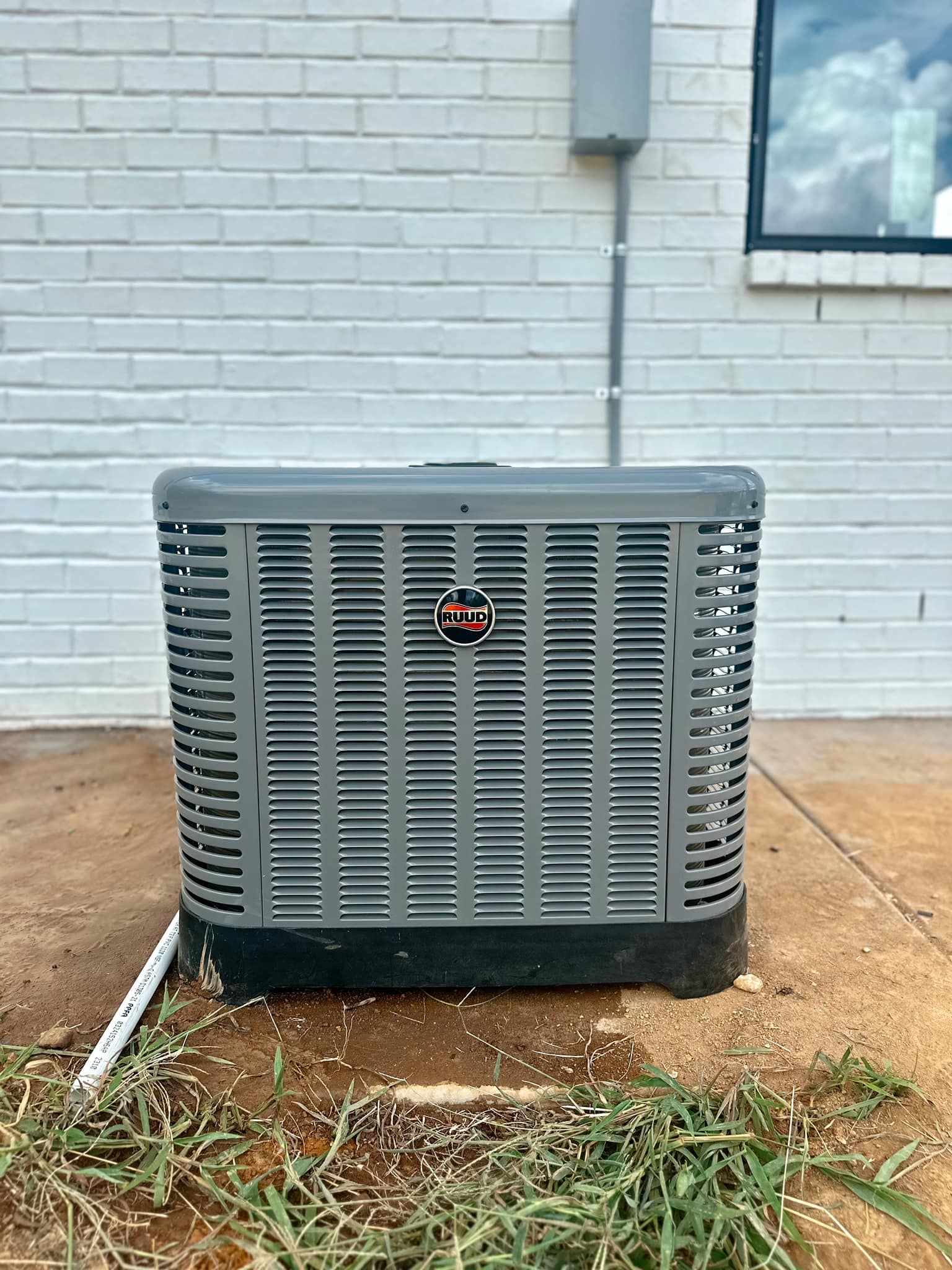 An air conditioner is sitting on the ground in front of a white brick building.