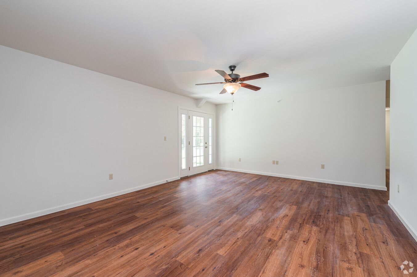 An empty living room with hardwood floors and a ceiling fan.