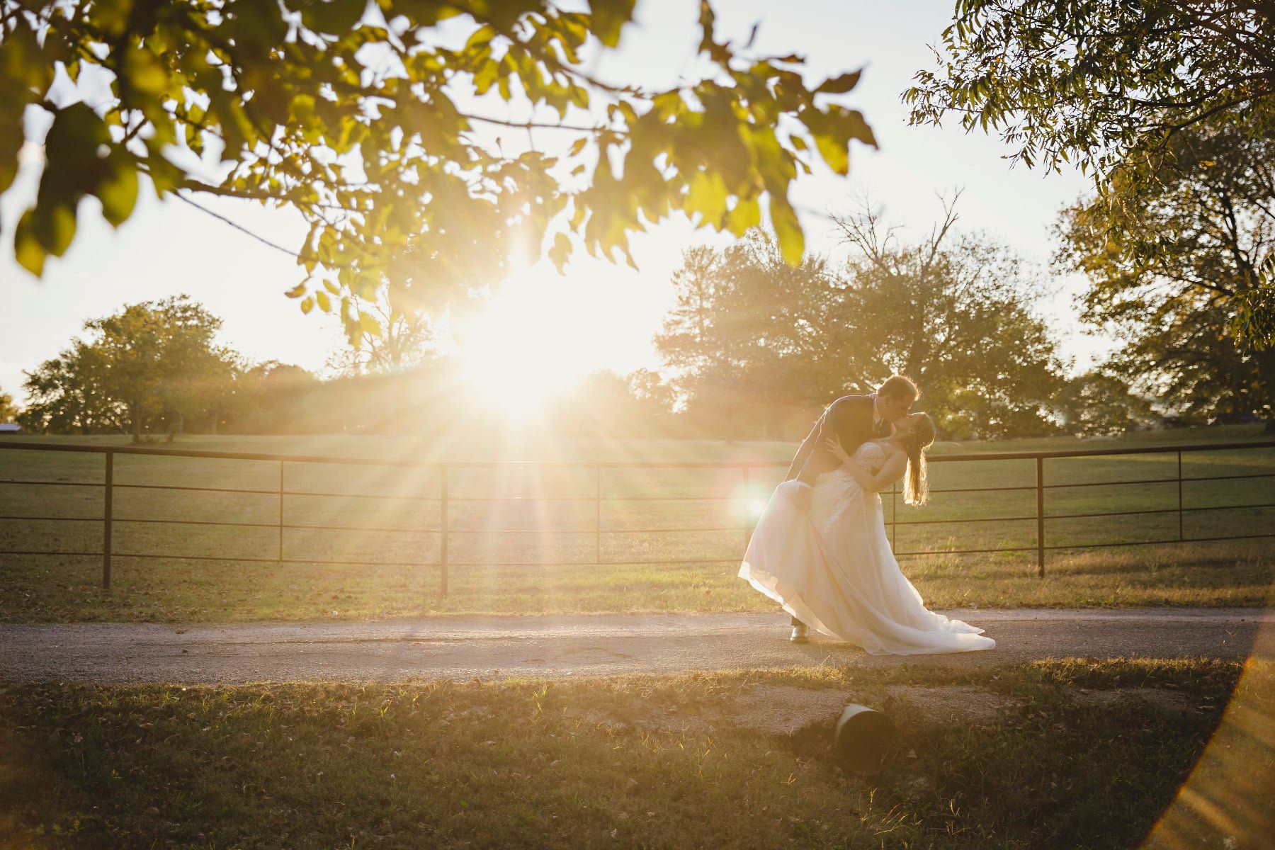 Bride and groom sharing a kiss as the sun sets behind them, with a scenic outdoor backdrop and a rus