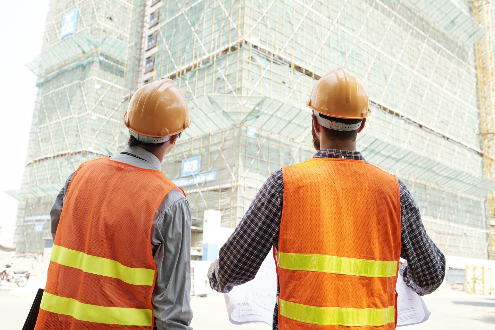 Two construction workers are looking at a blueprint at a construction site.