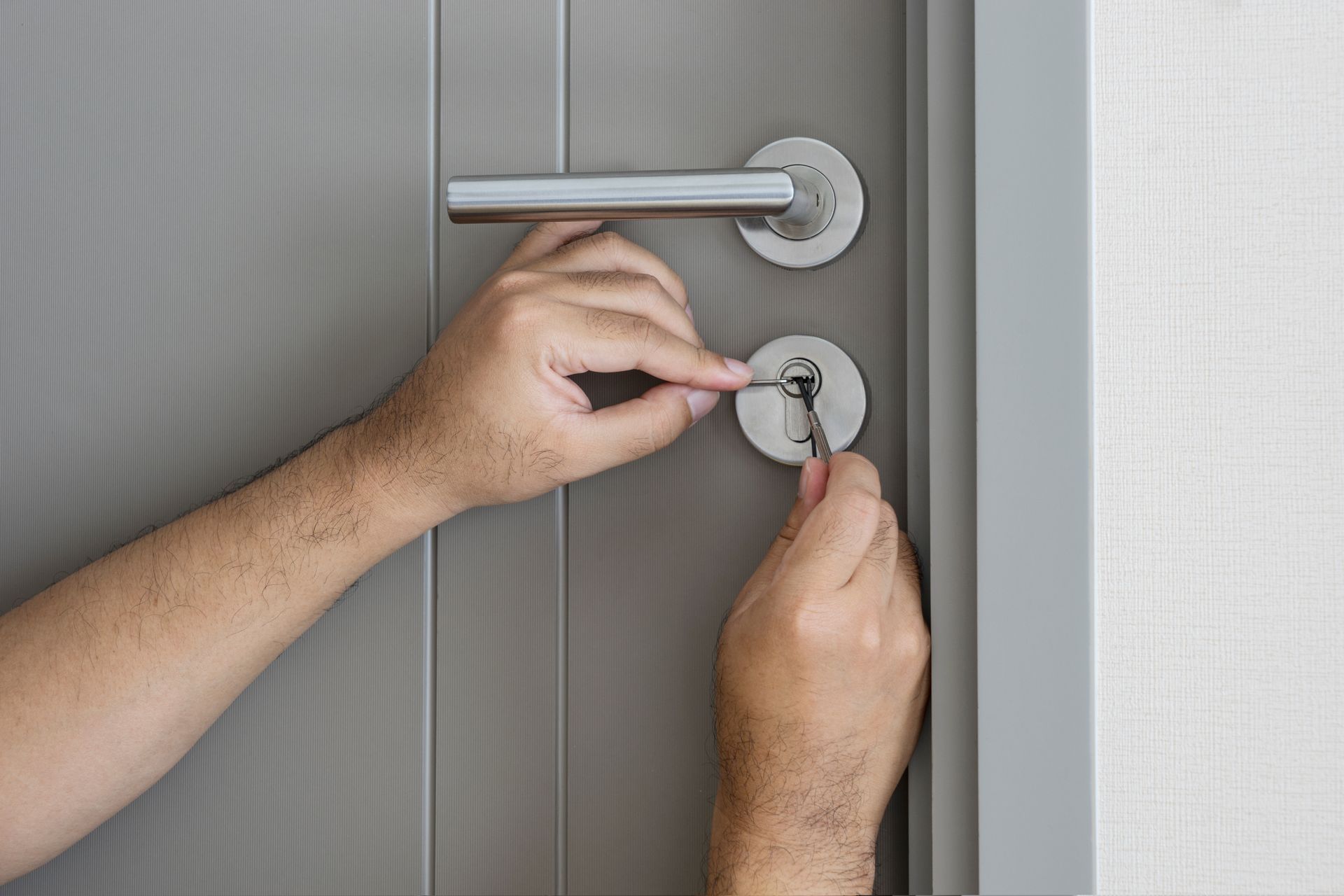 Hands installing a silver door lock on a gray door