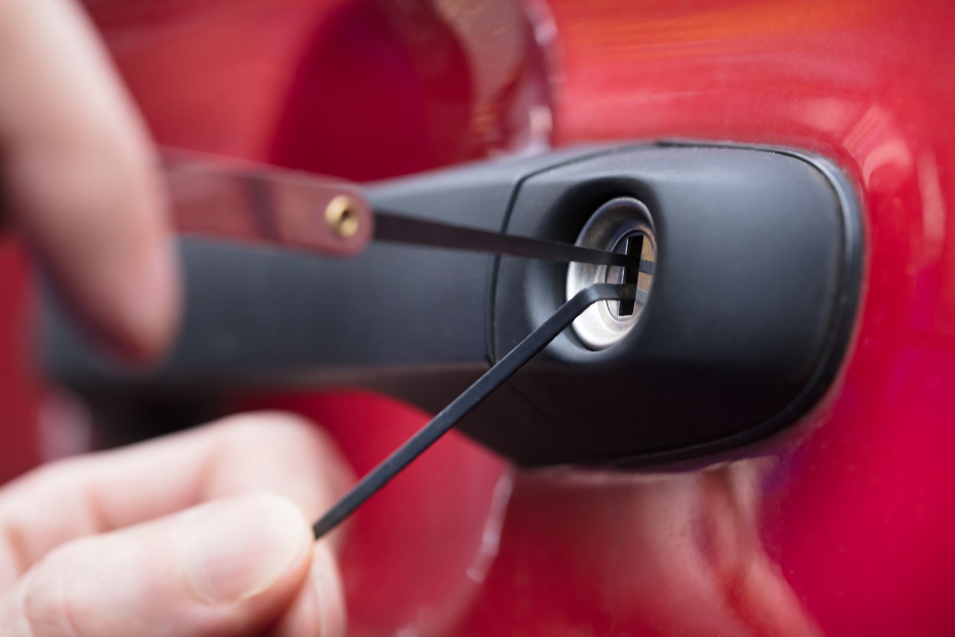 A person using lock picks to open a red car door lock