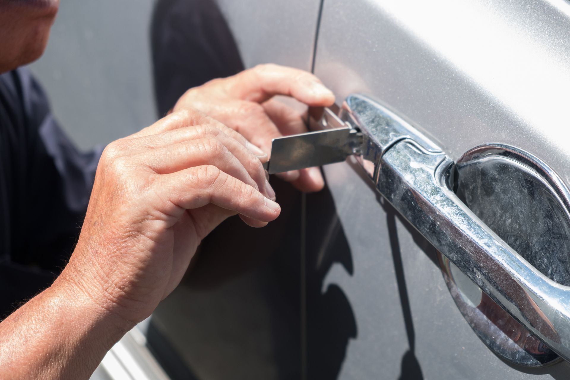 Hands using a key to unlock a silver car door handle
