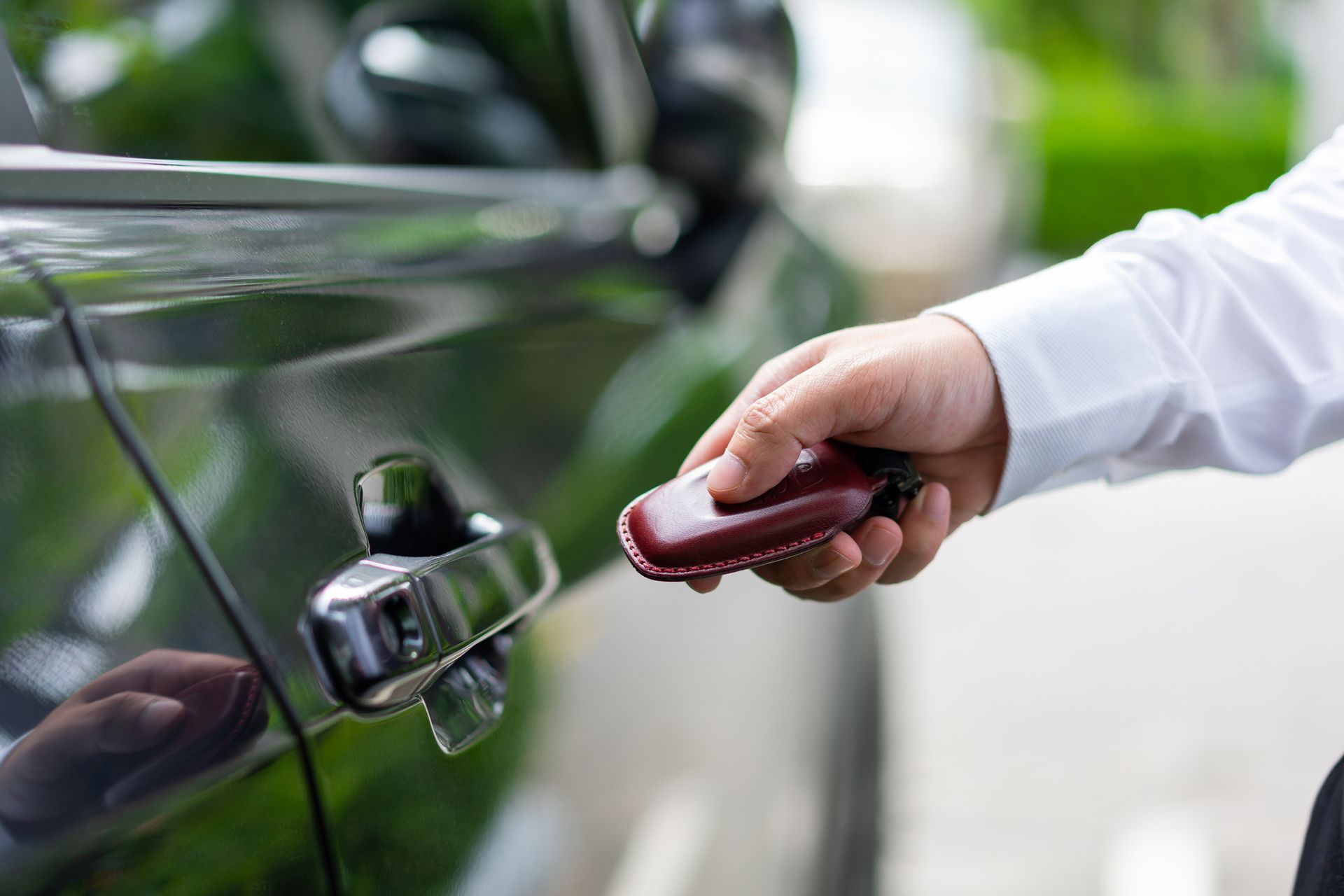 Hand with key unlocking a black car door handle outdoors.