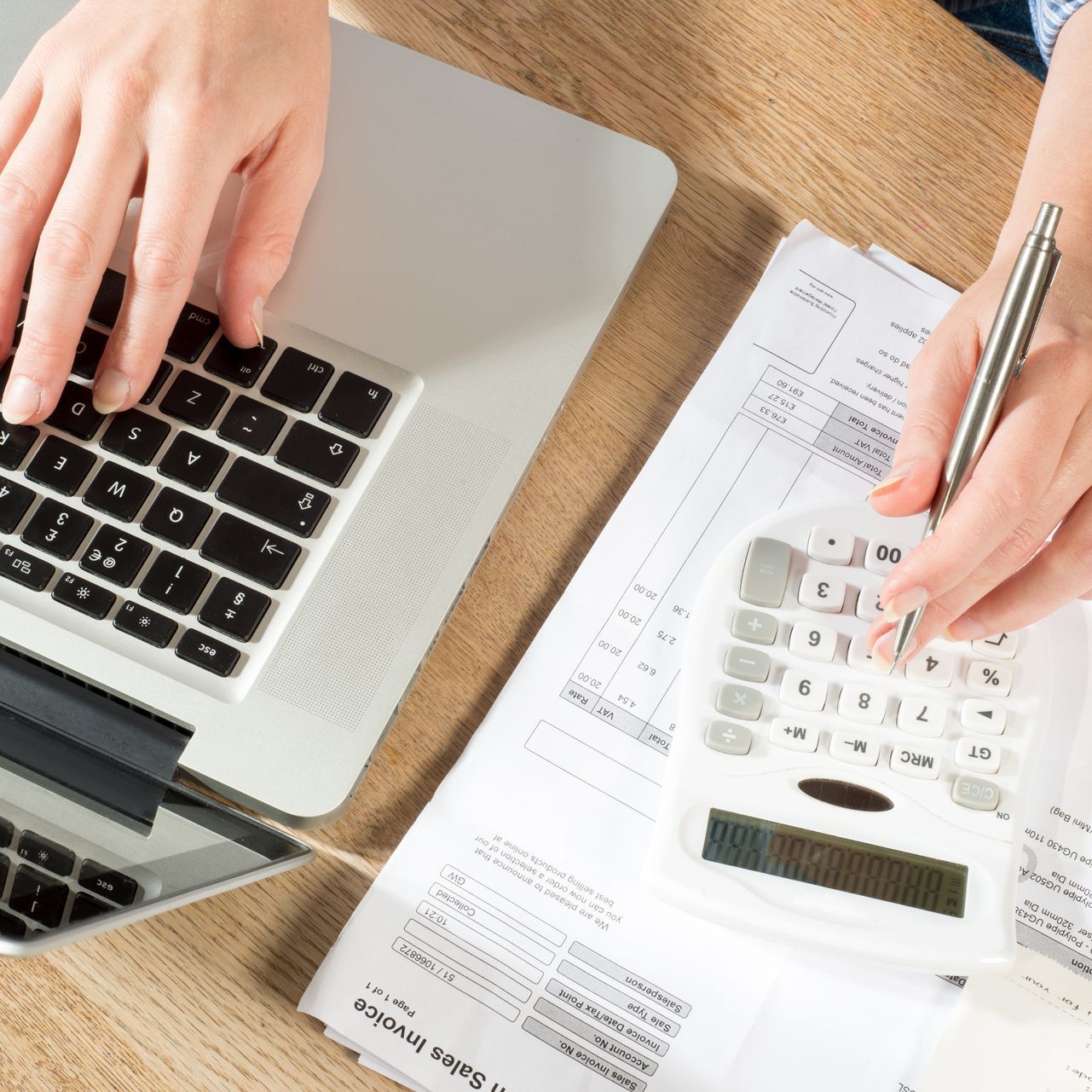 Hands typing on laptop and using calculator with documents on a desk.