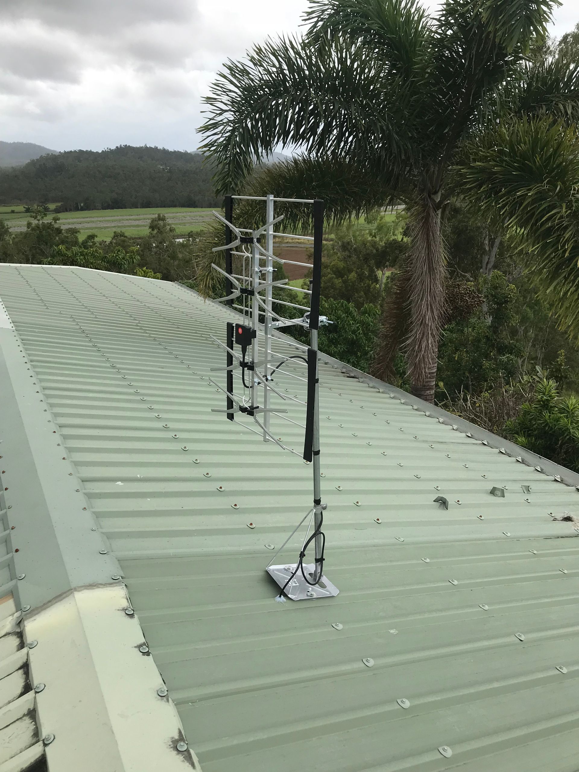TV antenna mounted on a green metal roof, with a rural landscape background.