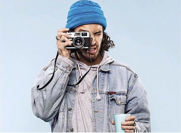 A man is taking a picture with a camera while holding a cup of coffee.