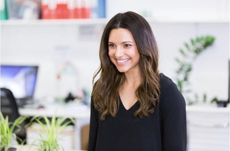 A woman in a black shirt is smiling in an office.