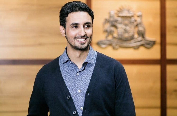 A man wearing a blue shirt and a black cardigan is smiling