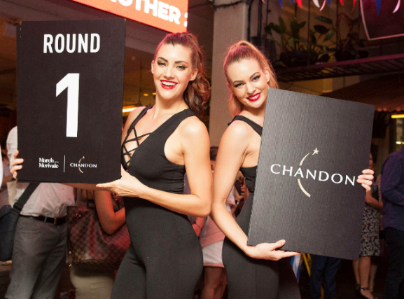 Two women holding signs that say round 1 and chandon
