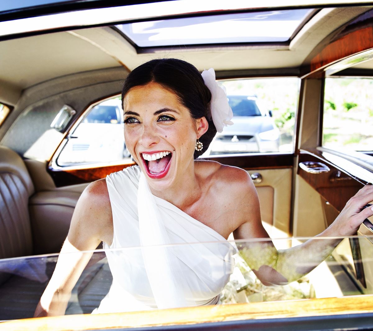 A woman in a white dress is laughing in a car