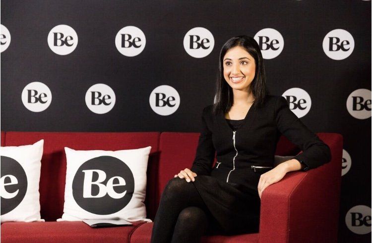 A woman sits on a red couch with white be pillows