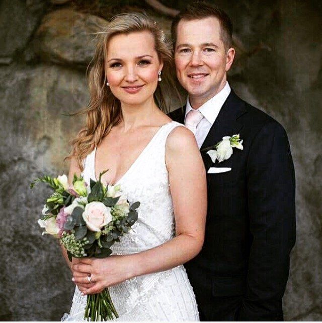 A bride and groom are posing for a picture while the bride is holding a bouquet of flowers.