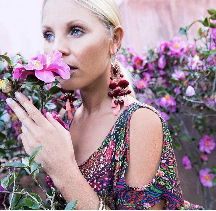 A woman in a floral dress smells a pink flower