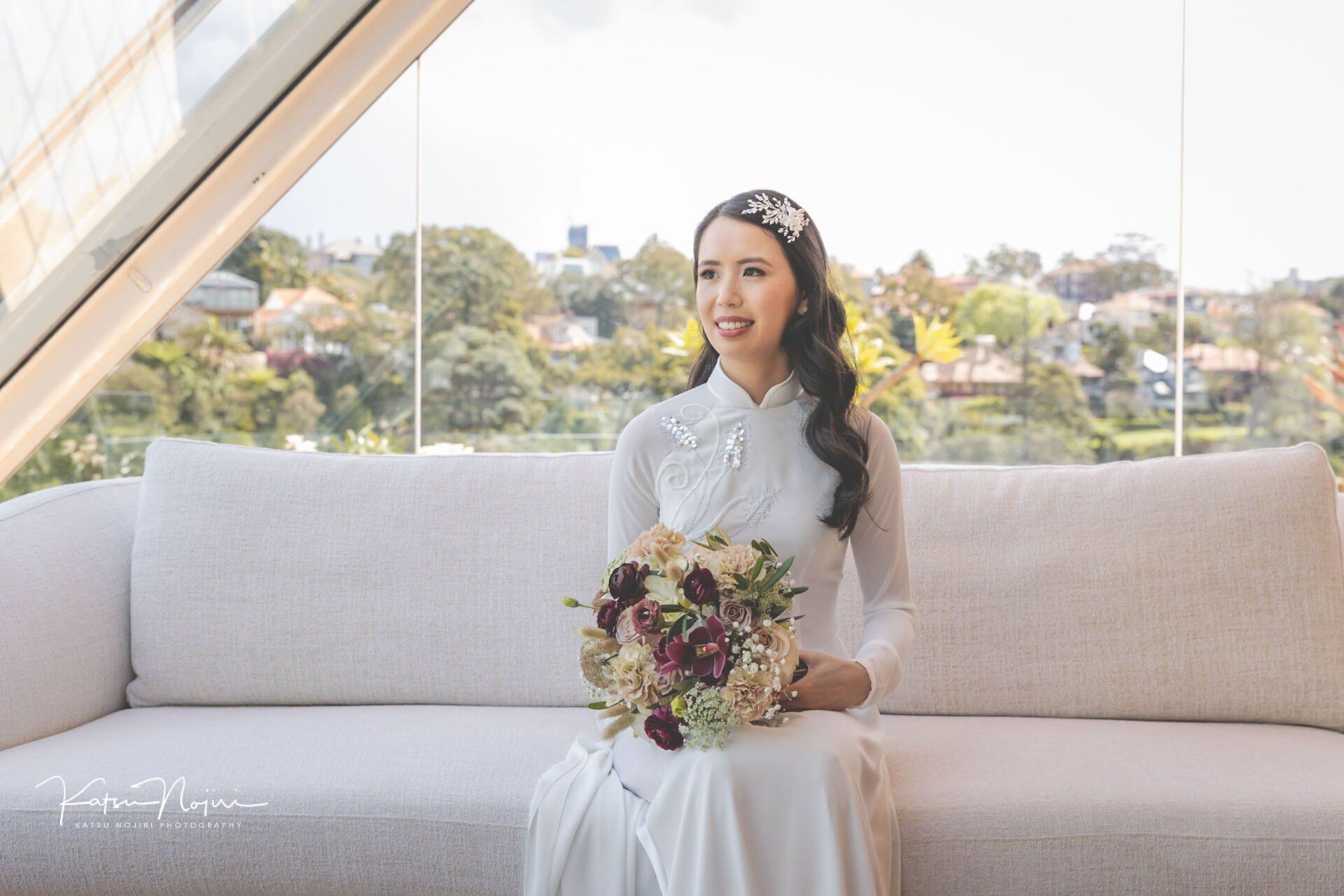 A woman in a wedding dress is sitting on a couch holding a bouquet of flowers.