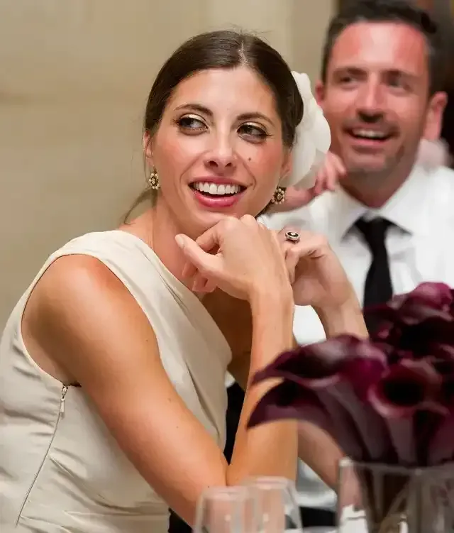 A woman in a white dress is smiling while sitting at a table with a man in a suit and tie.