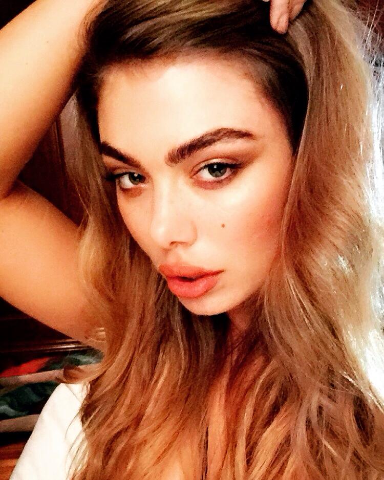 A woman with long hair is taking a selfie with her hand in her hair.