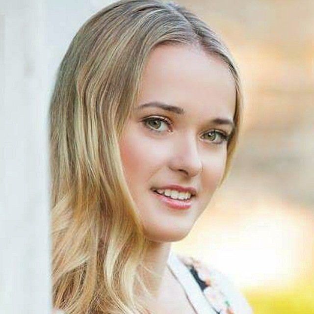 A close up of a woman 's face with long blonde hair and green eyes.