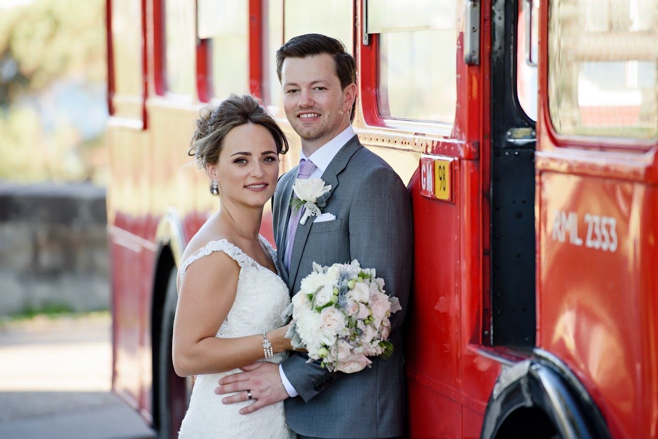 A bride and groom pose in front of a red bus