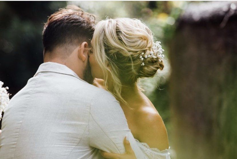 A bride and groom are hugging each other in the woods.
