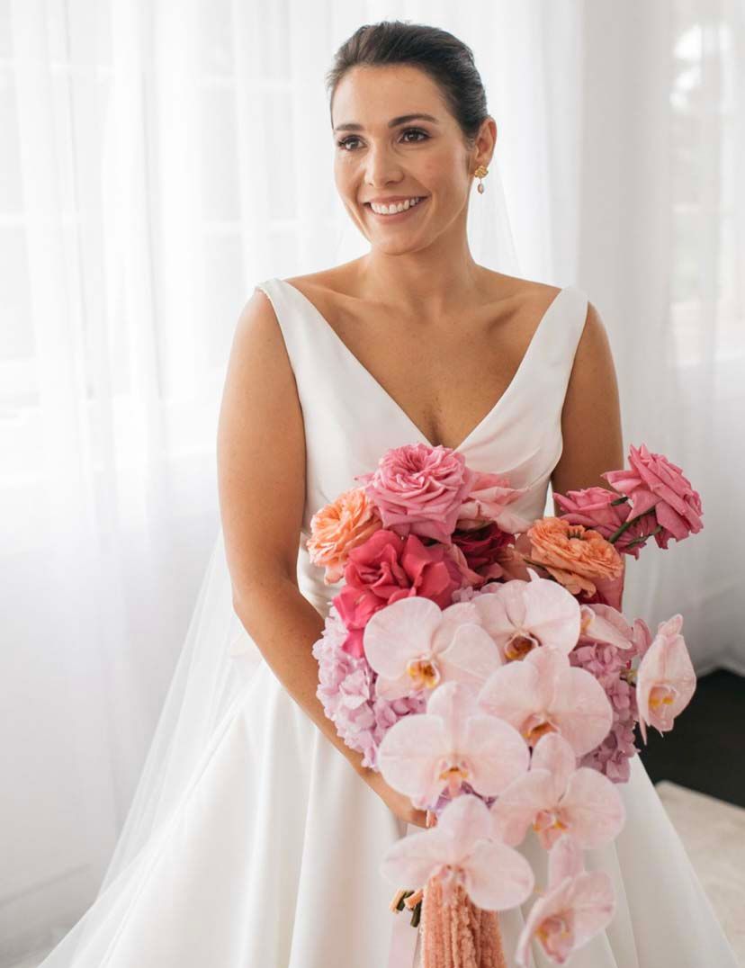 A bride in a white dress is holding a bouquet of pink flowers.
