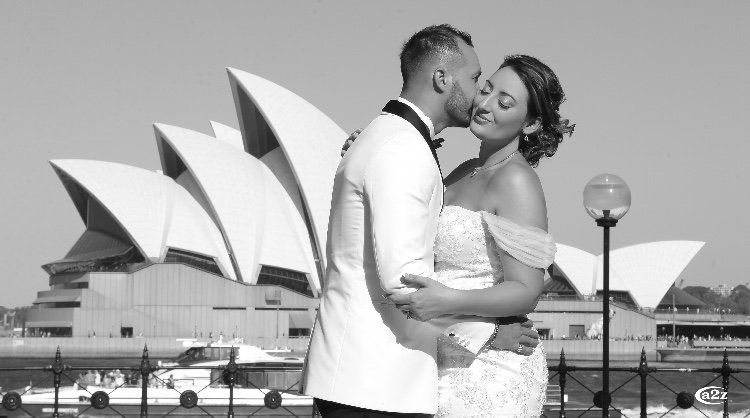 A black and white photo of a bride and groom kissing in front of the opera house.