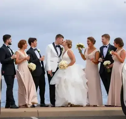 A bride and groom are kissing in front of their wedding party.