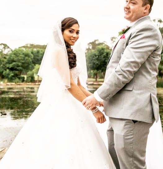A bride and groom are holding hands in front of a lake.