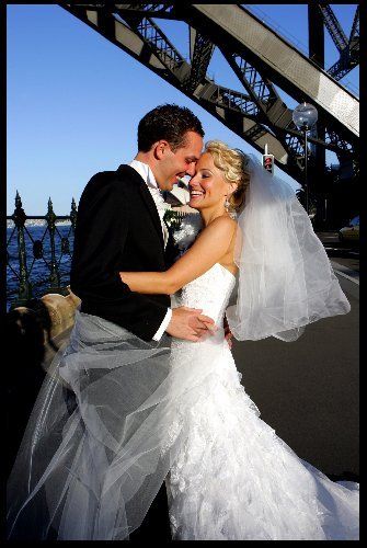 A bride and groom are posing for a picture under a bridge