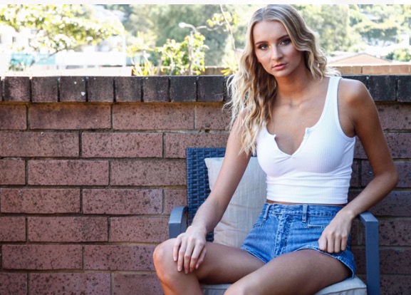 A woman in a white tank top and shorts is sitting in a chair