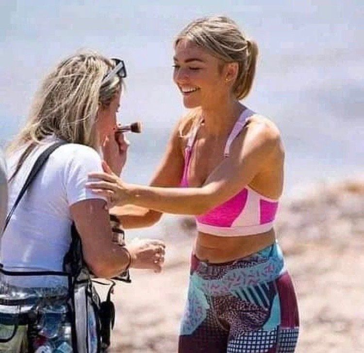 A woman is applying makeup to another woman 's face on the beach.