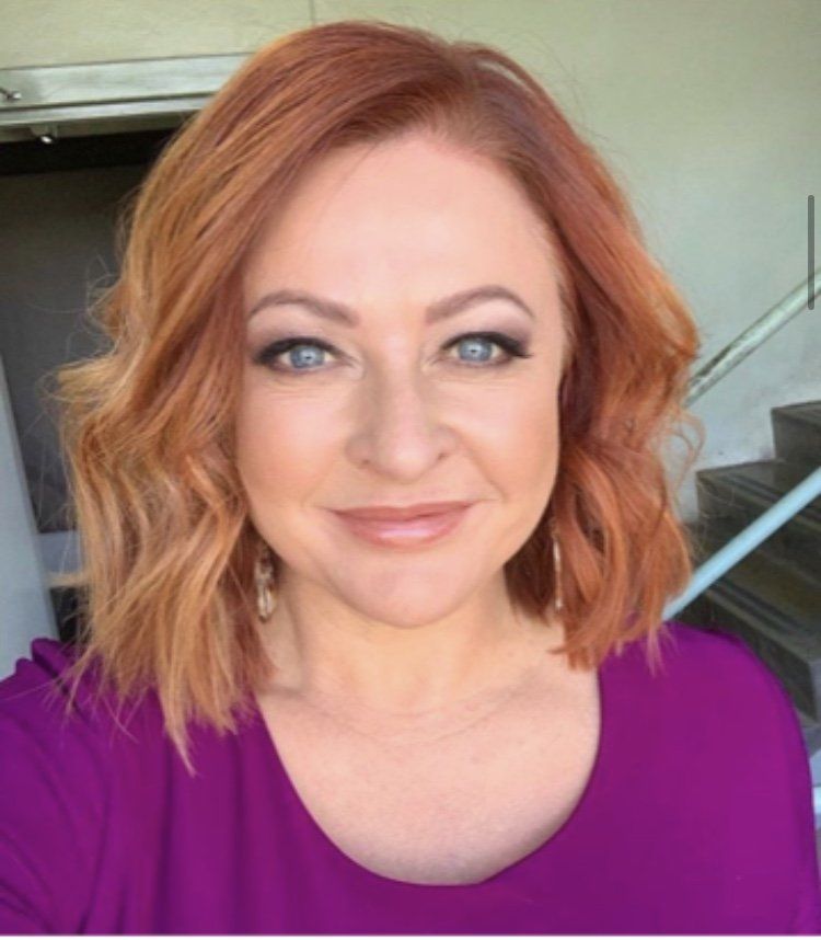 A woman with red hair and blue eyes is wearing a purple shirt.