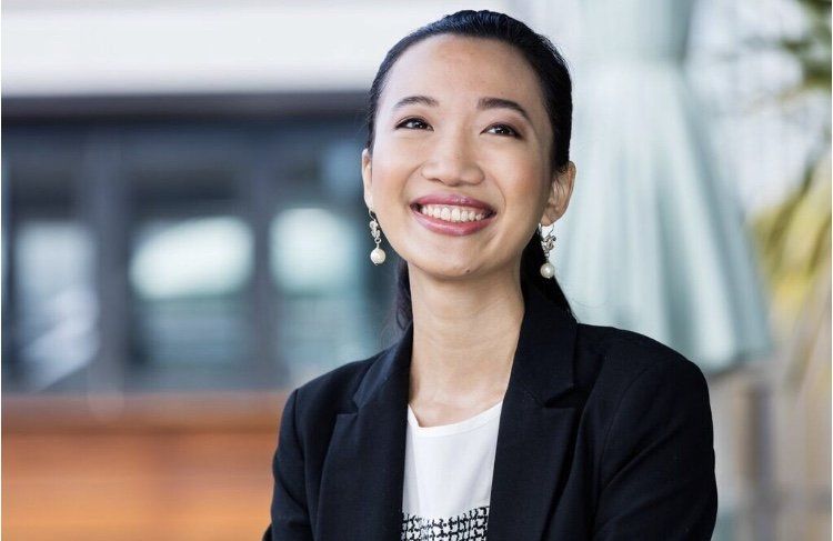 A woman in a black jacket and white shirt is smiling.