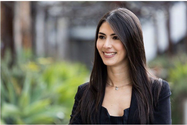 A woman with long dark hair is smiling and wearing a black jacket.
