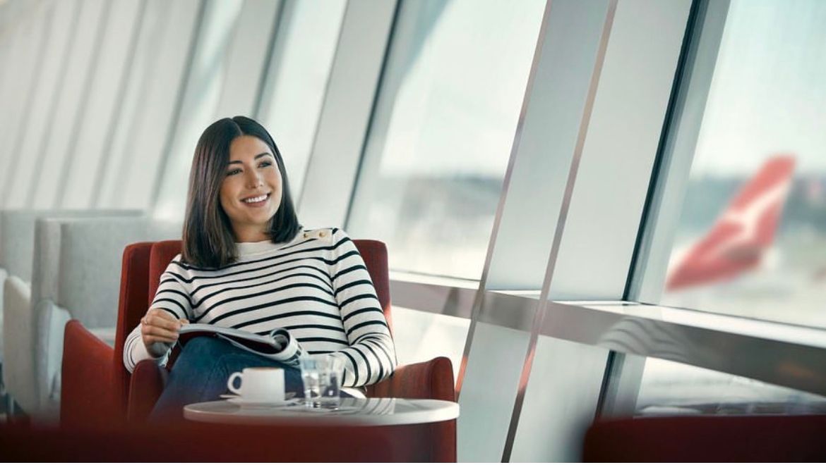 A woman is sitting in a chair at an airport reading a magazine.