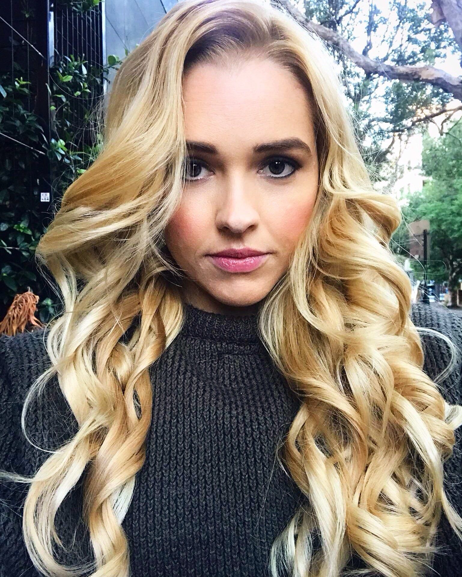 A woman with long blonde hair is wearing a grey sweater