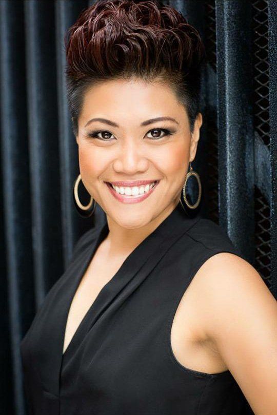 A woman wearing a black top and gold hoop earrings smiles for the camera