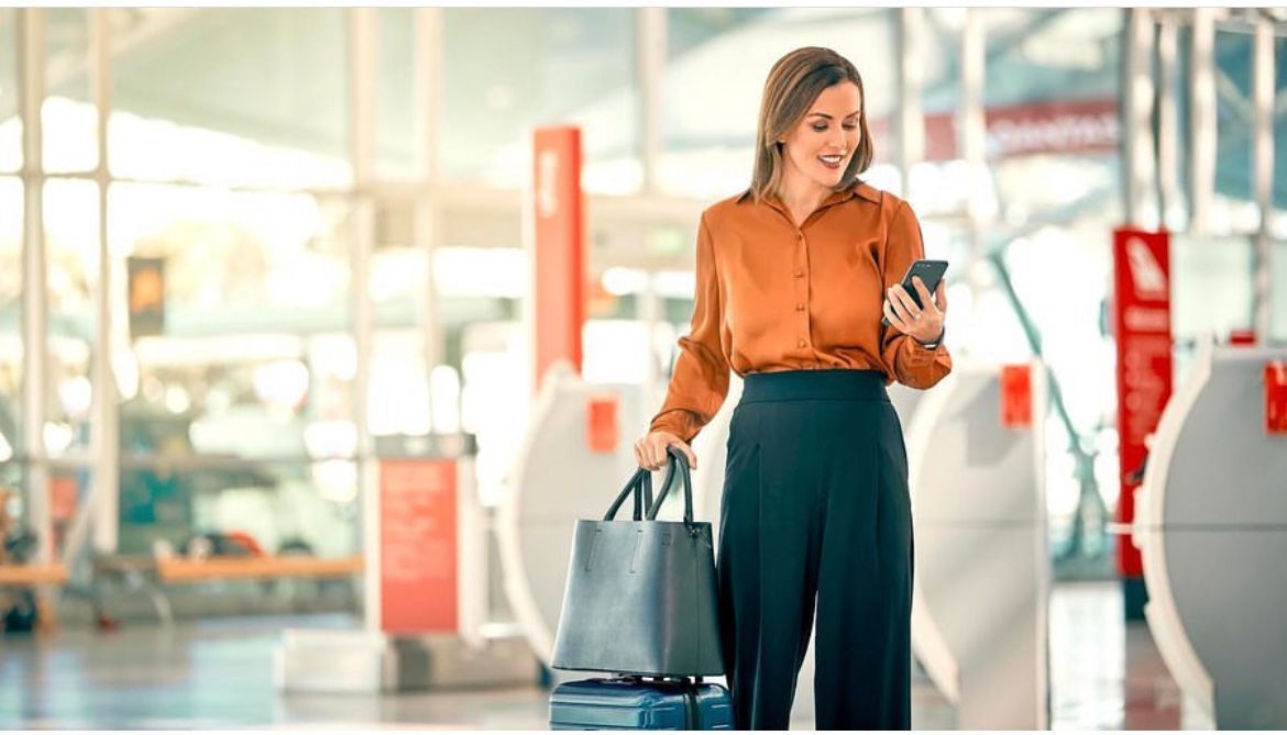 A woman is holding a suitcase and looking at her phone at an airport.