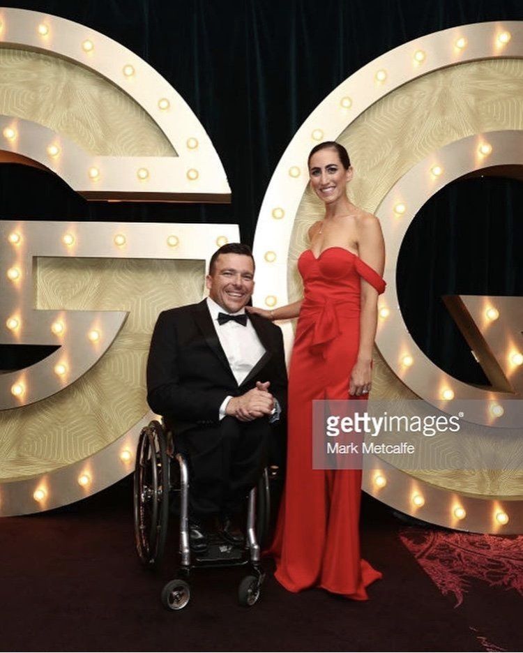 A man in a wheelchair is standing next to a woman in a red dress