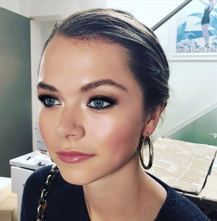 A woman wearing hoop earrings is standing in front of a poster that says sur la cote d' az