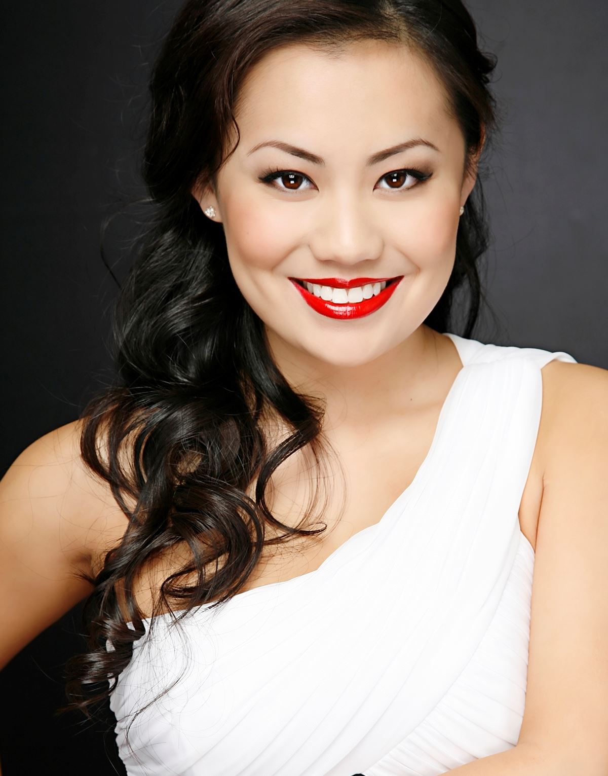 A woman wearing a white dress and red lipstick smiles for the camera
