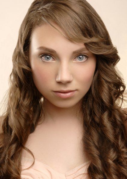 A woman with long brown hair and blue eyes is wearing a pink dress