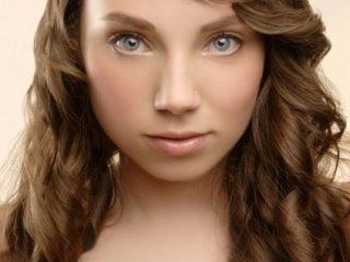 A woman with long brown hair and blue eyes is looking at the camera.