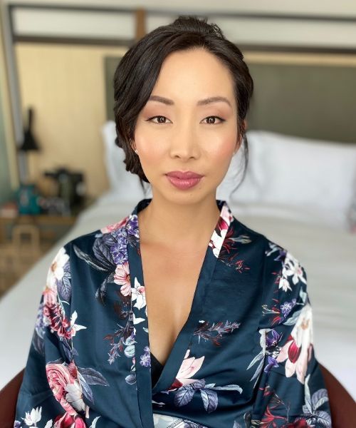 A woman in a floral robe is sitting in front of a bed.